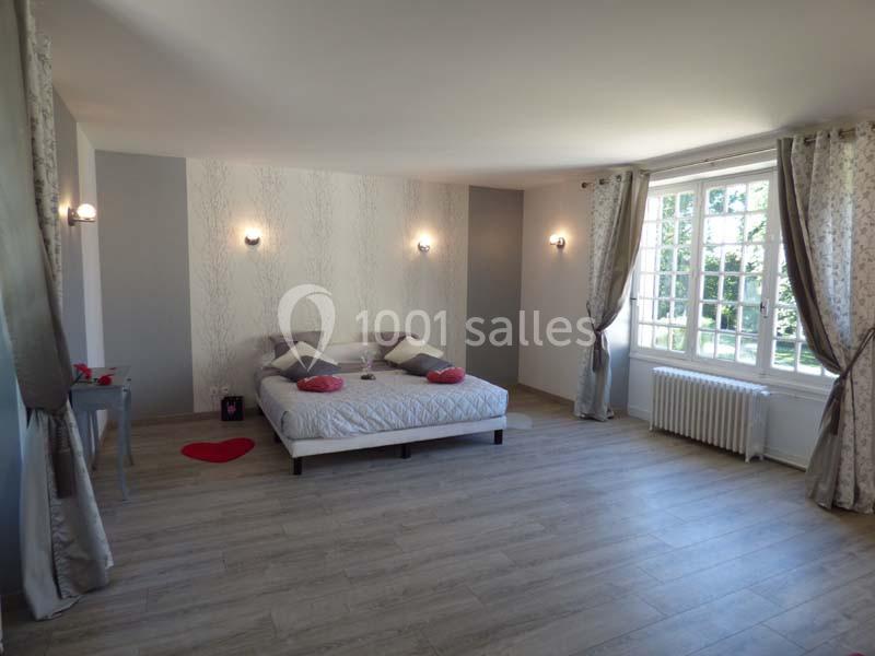 Chambre lumineuse avec lit double, parquet clair, murs décorés, rideaux beige et grande fenêtre donnant sur un jardin.