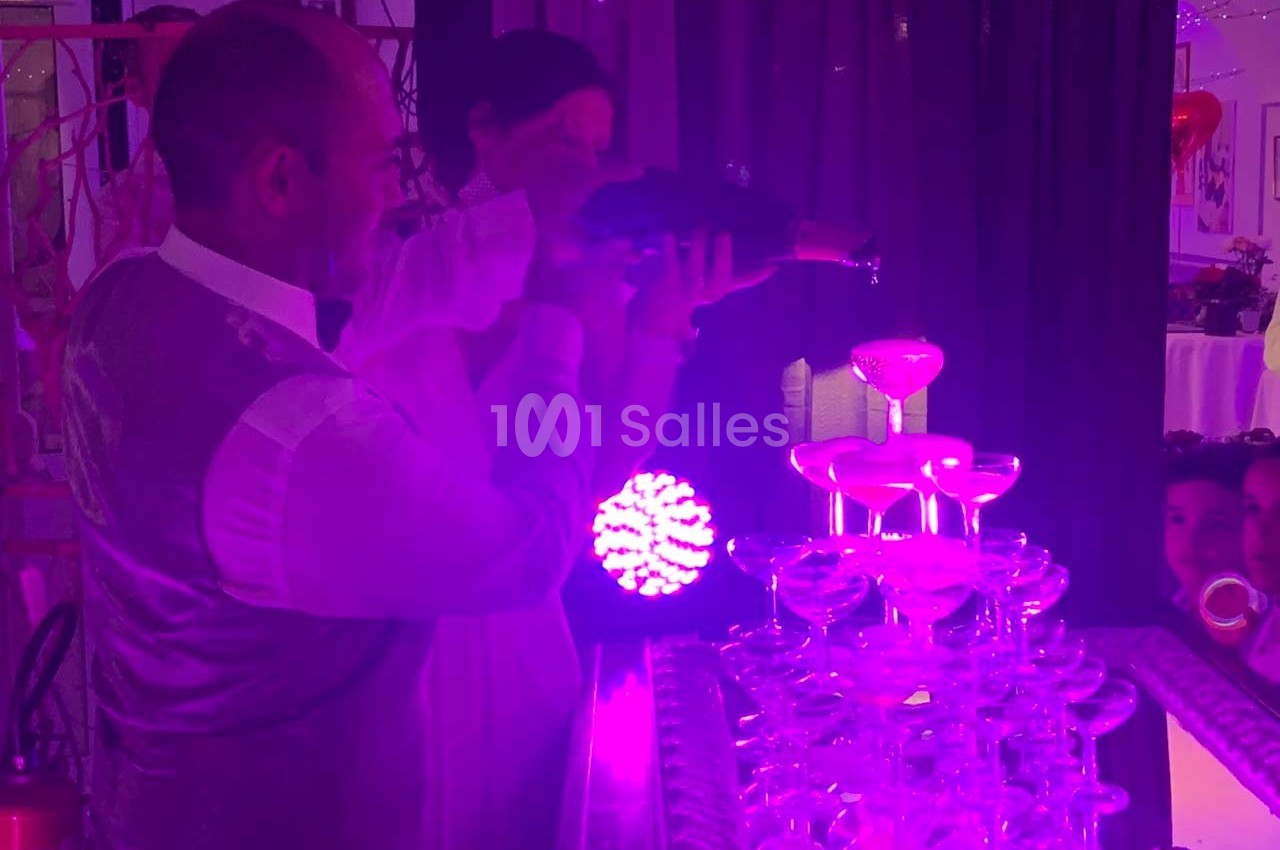 Un serveur verse du champagne dans une pyramide de coupes éclairée par une lumière violette.