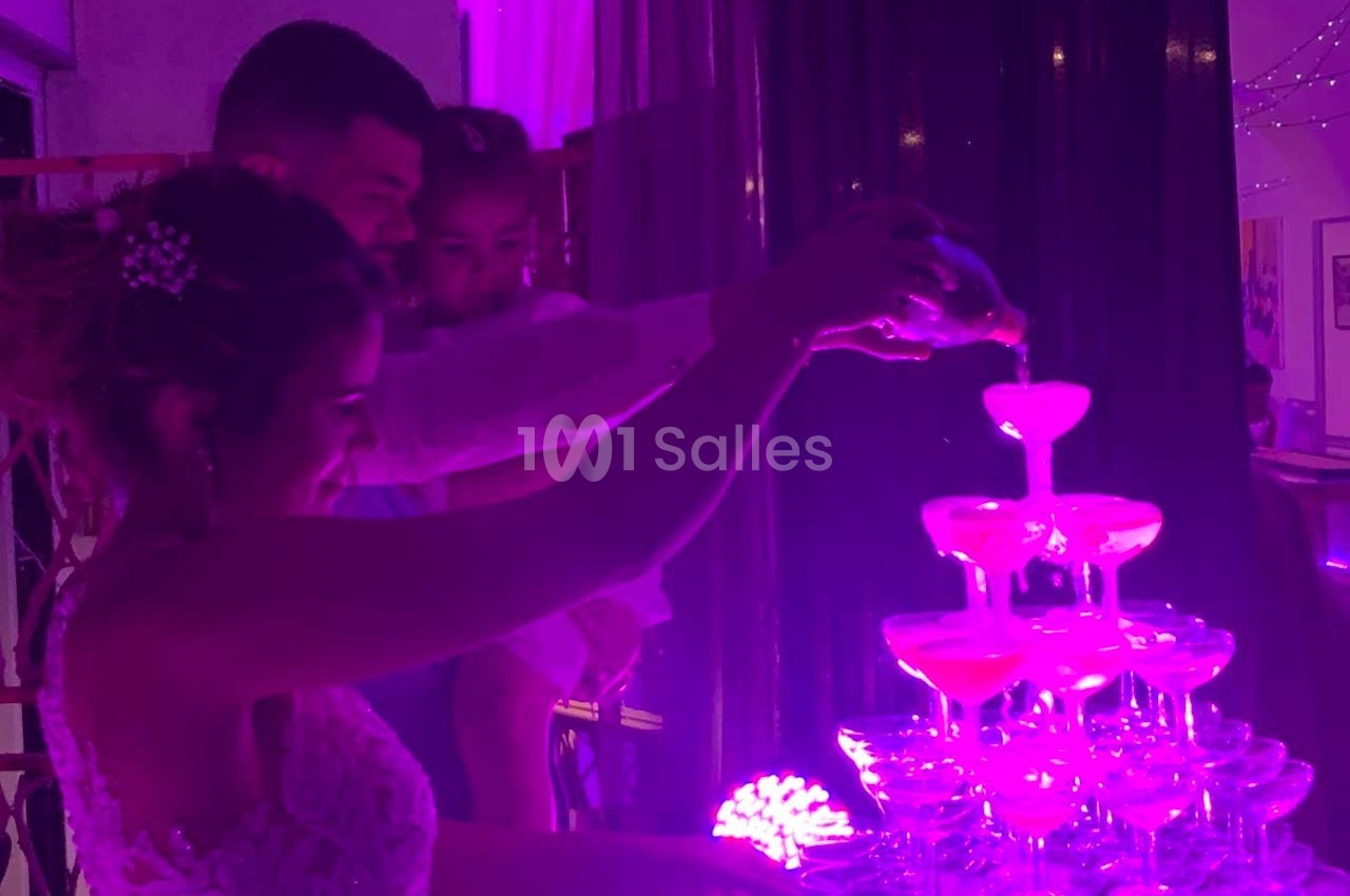 Un couple verse un liquide dans une fontaine de coupes illuminée de lumière violette, avec un enfant dans leurs bras.