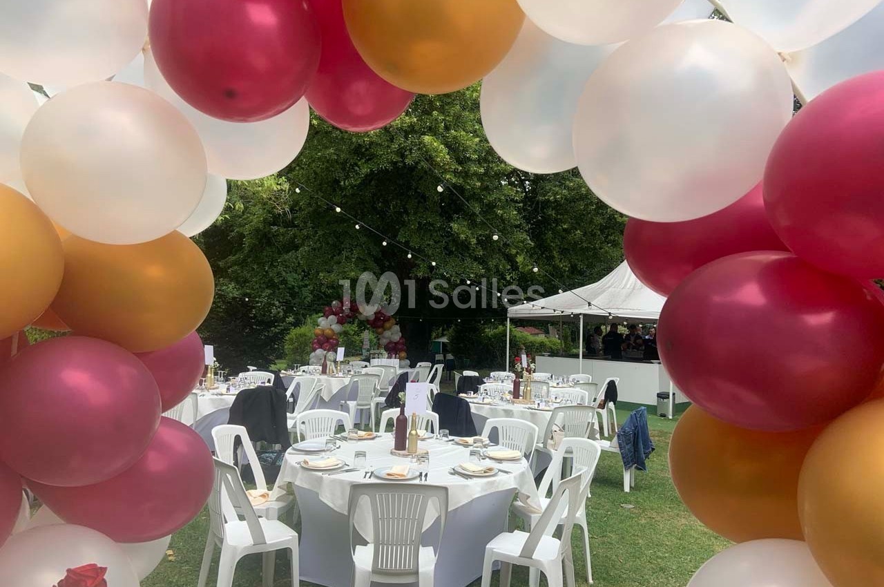 Arche de ballons colorés encadrant des tables dressées pour un événement en plein air dans un jardin.