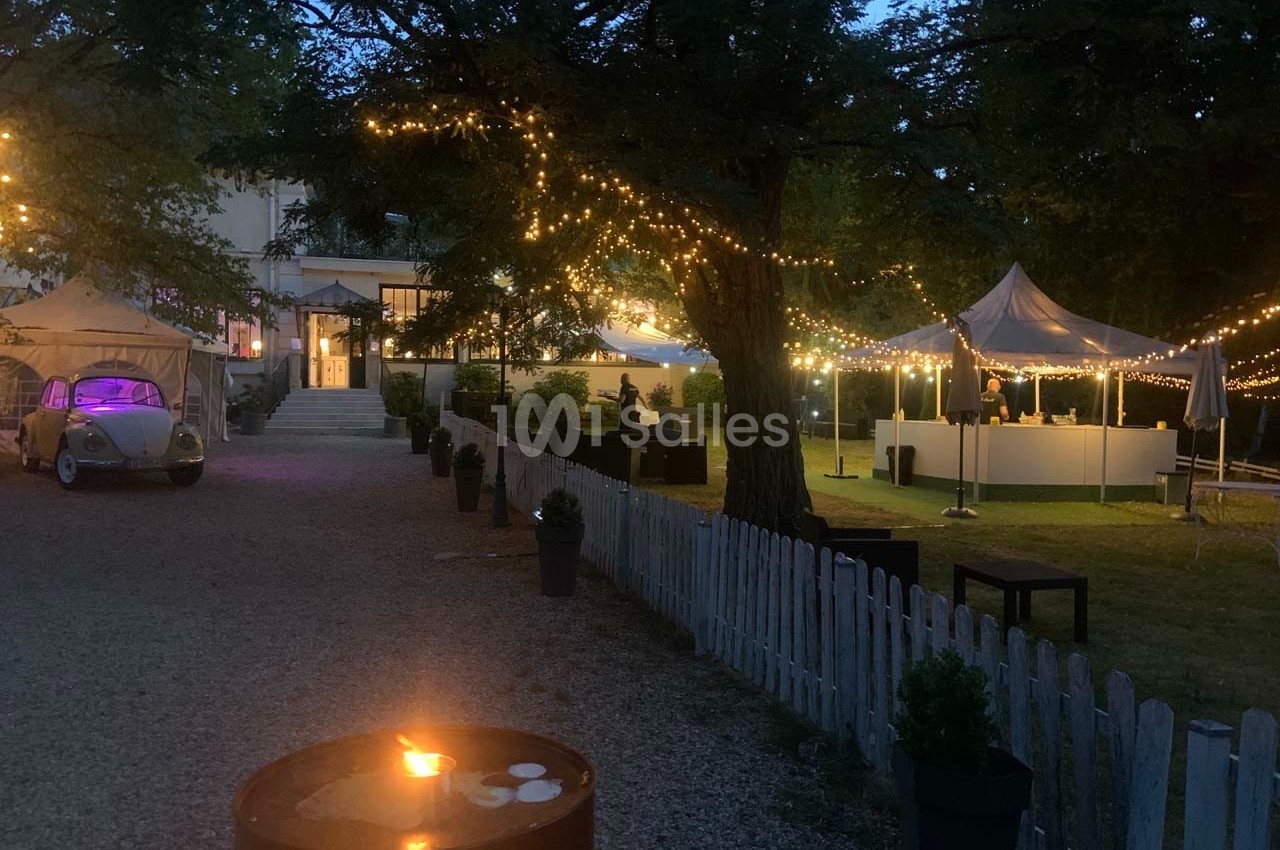 Jardin éclairé en soirée avec guirlandes lumineuses, tentes blanches et une voiture ancienne stationnée.