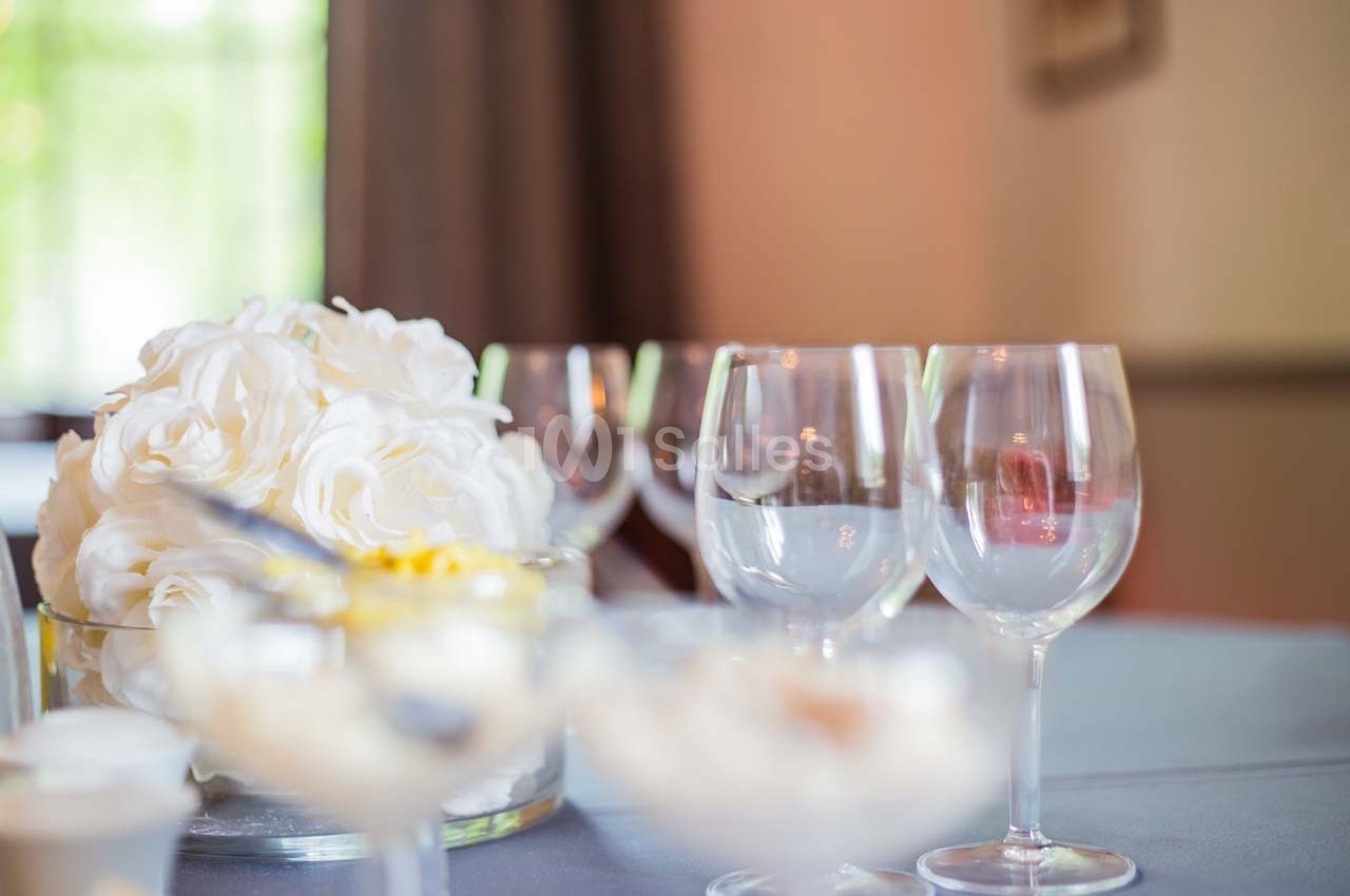 Bouquet de fleurs blanches et verres à pied disposés sur une table grise dans un cadre lumineux.