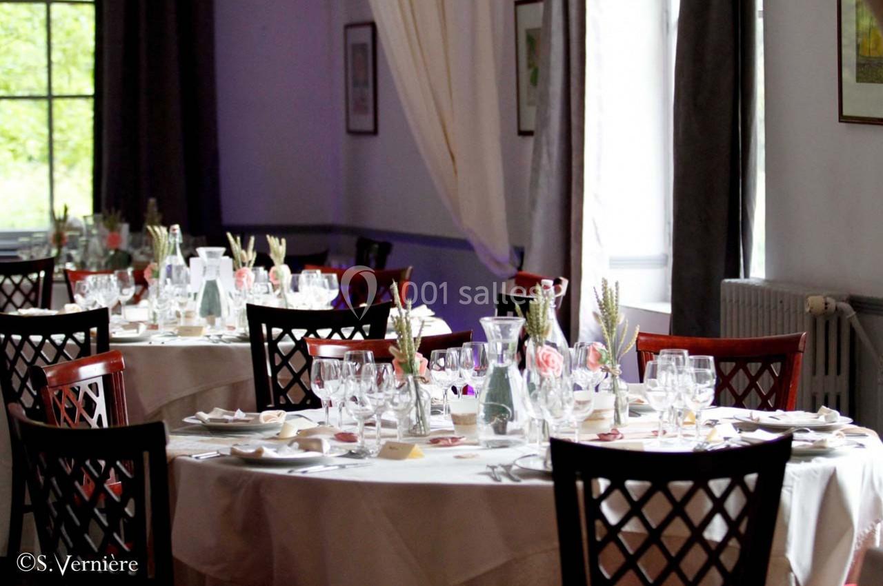 Salle de réception élégante avec des tables rondes dressées, nappes blanches, verres et décorations florales.