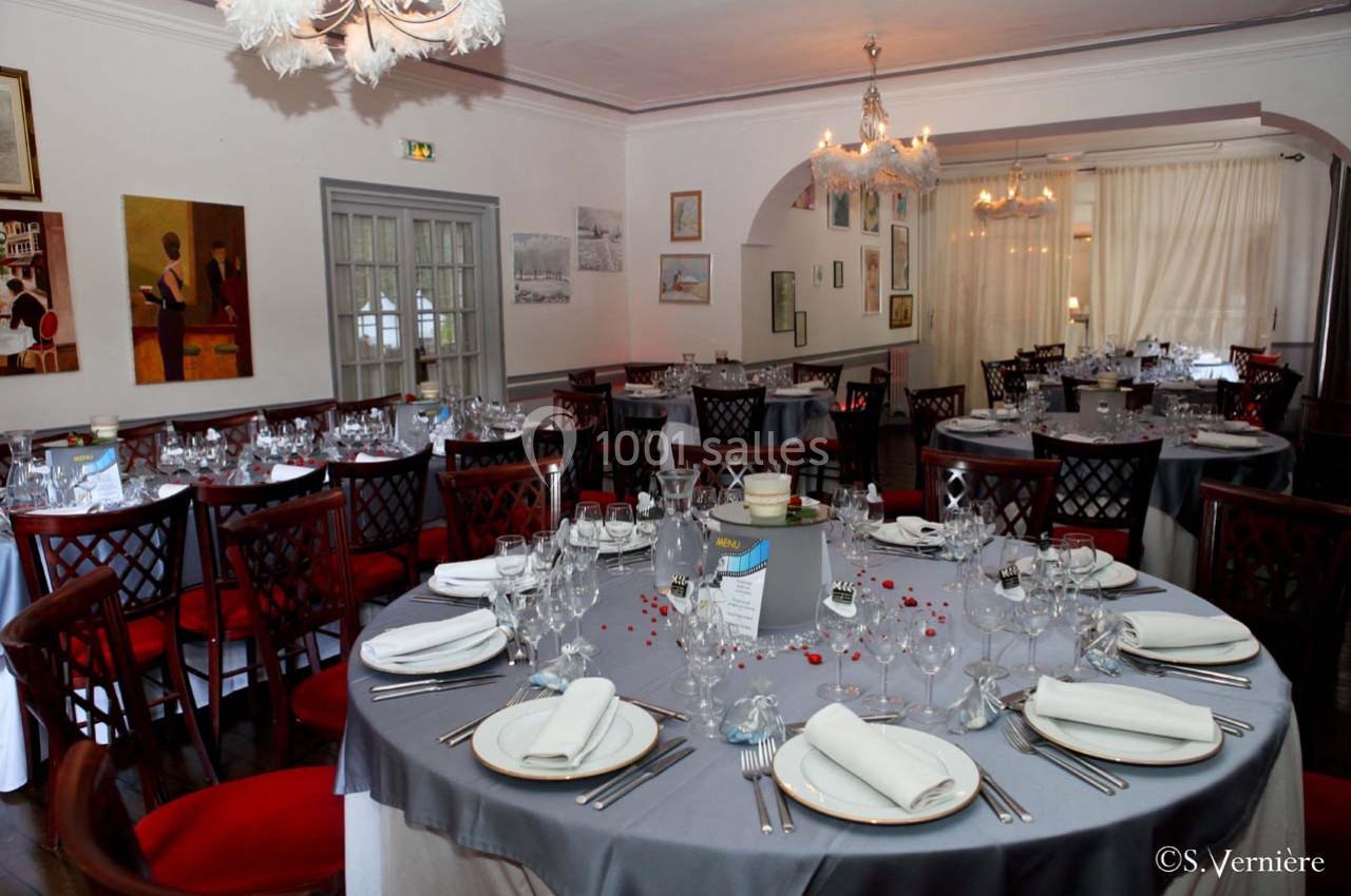 Salle de restaurant élégante avec tables rondes dressées, nappes grises, serviettes blanches et décoration soignée.