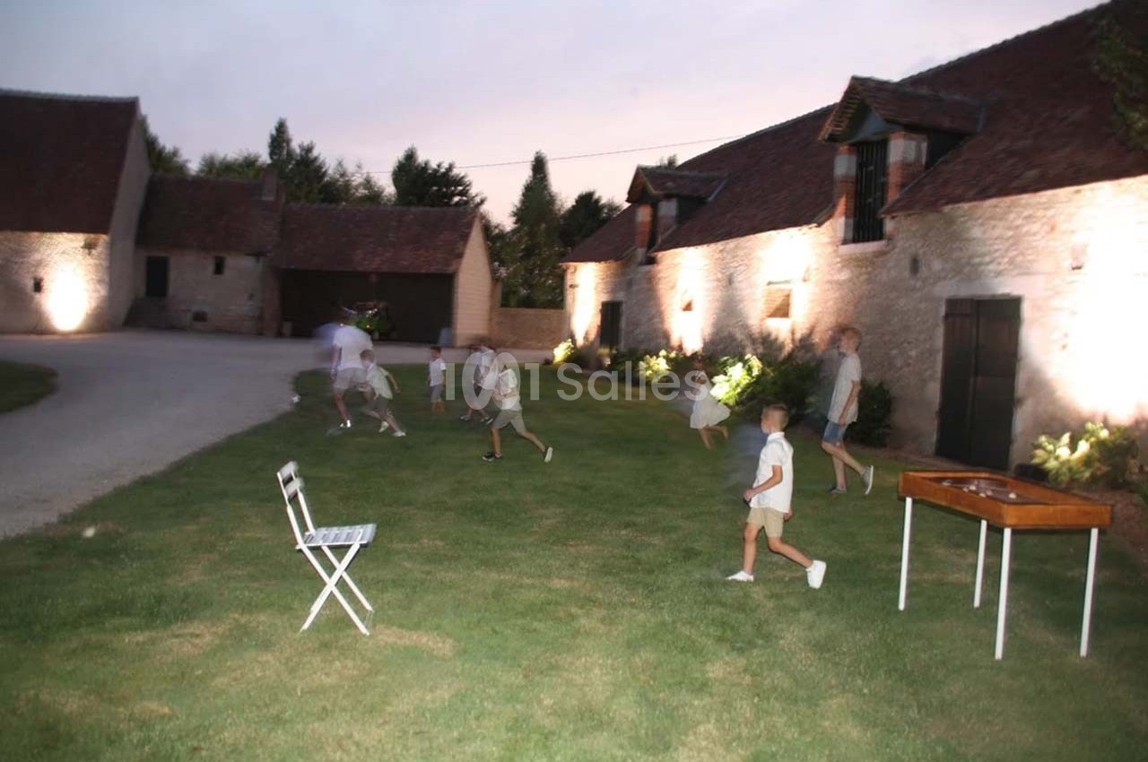 Des enfants jouent sur une pelouse au crépuscule devant des bâtiments en pierre éclairés.