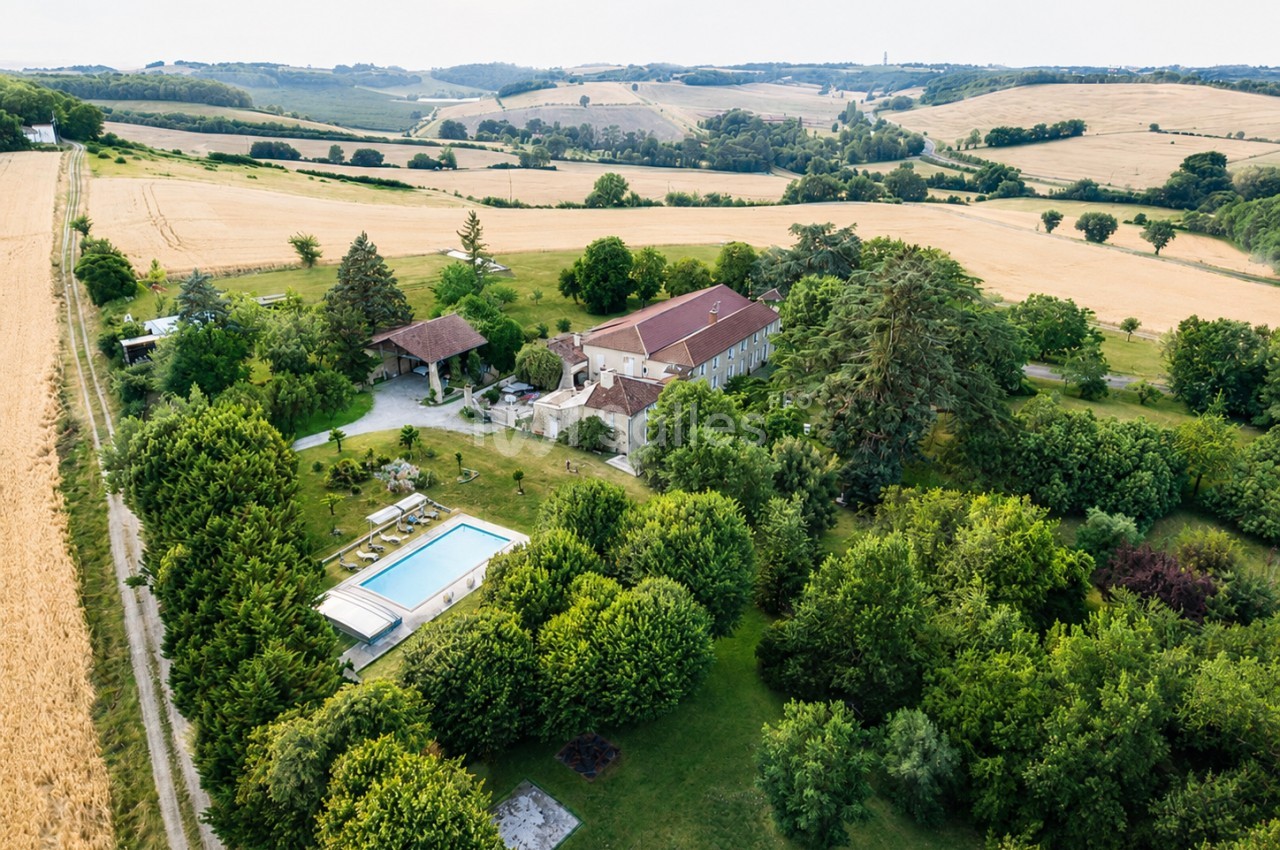 Vue aérienne d'une maison en pierre avec piscine, entourée de jardins et de champs dans un paysage vallonné.