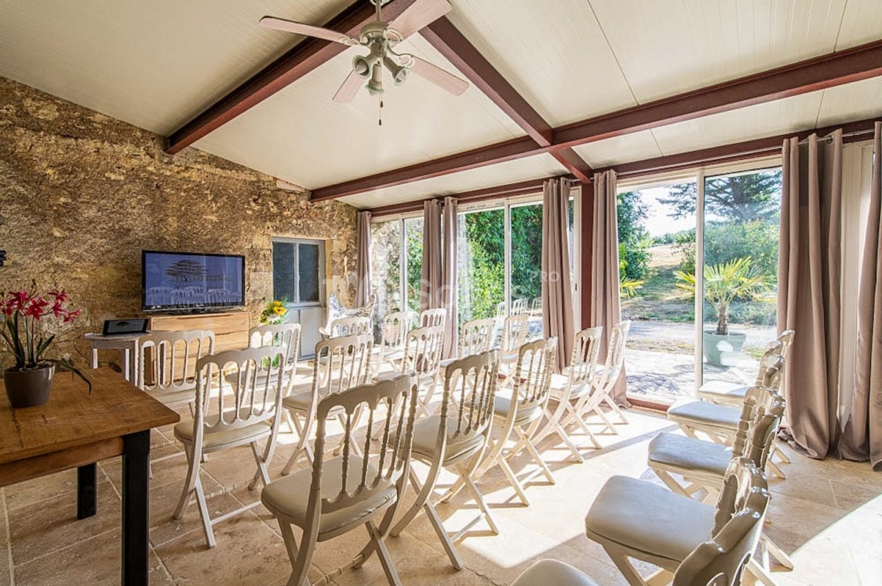 Salle lumineuse avec chaises blanches alignées, grandes baies vitrées donnant sur un jardin verdoyant.