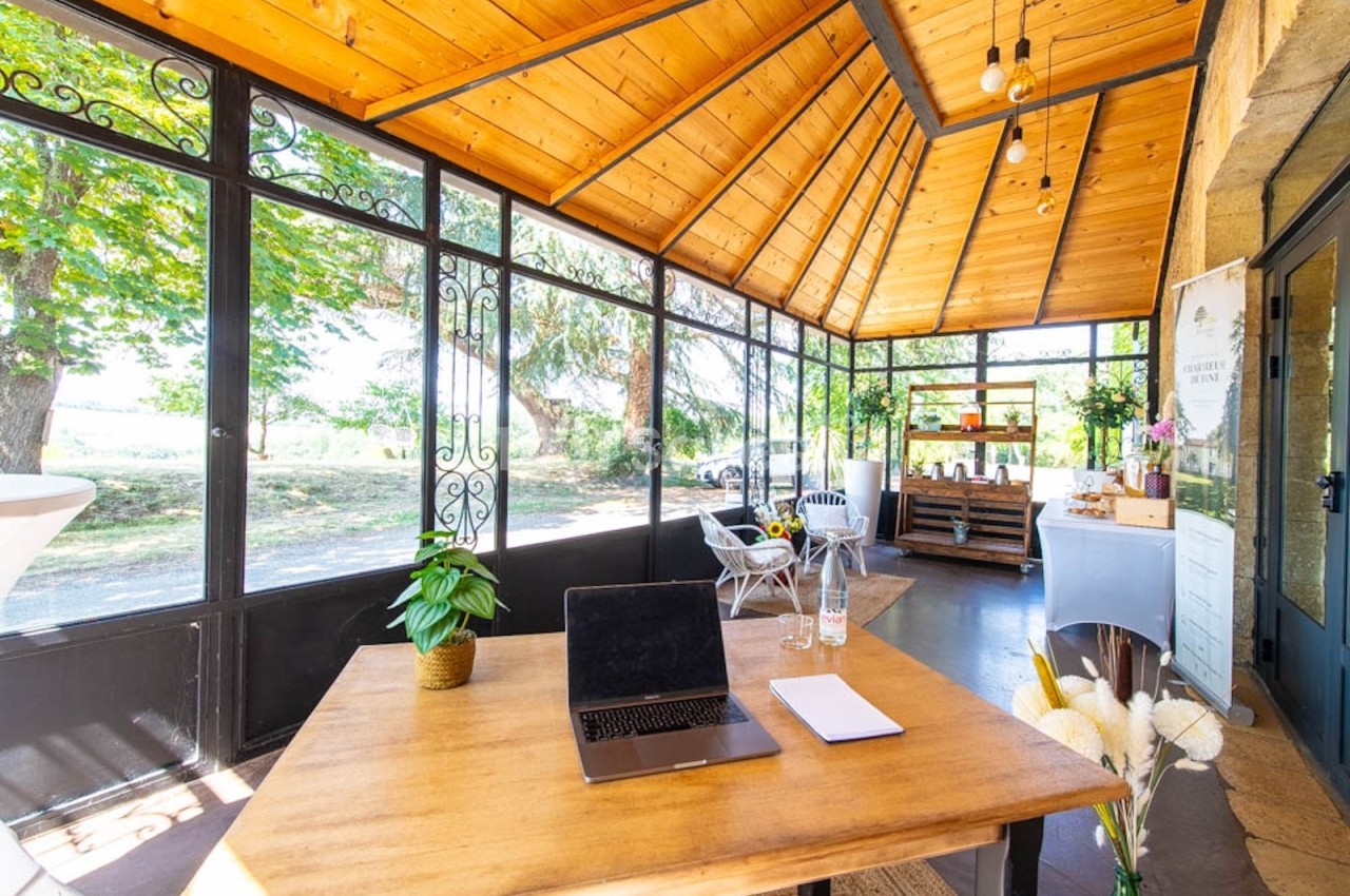 Salle lumineuse avec toit en bois, grandes baies vitrées, table avec ordinateur portable et vue sur un espace extérieur…