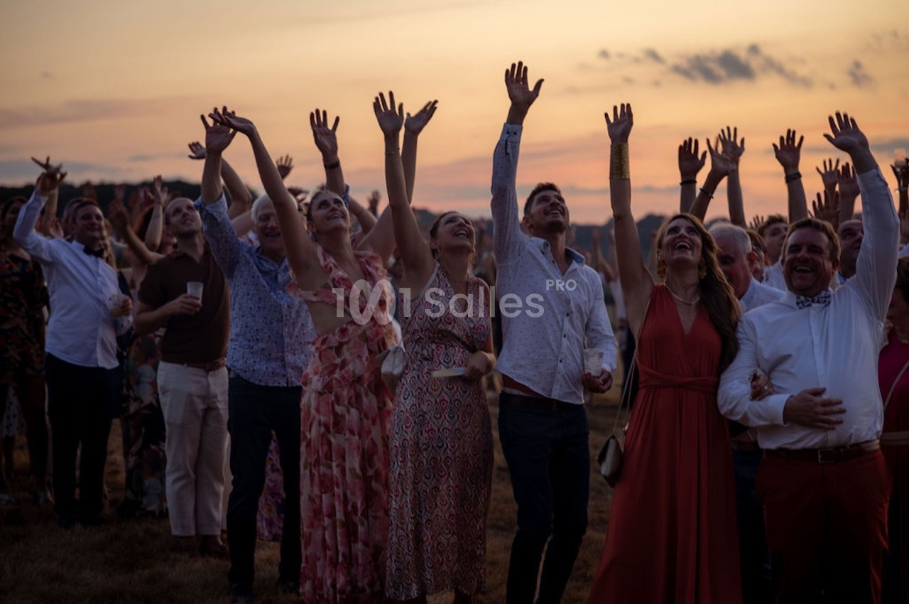 Groupe de personnes levant les bras en l'air lors d'un événement en plein air au coucher du soleil.