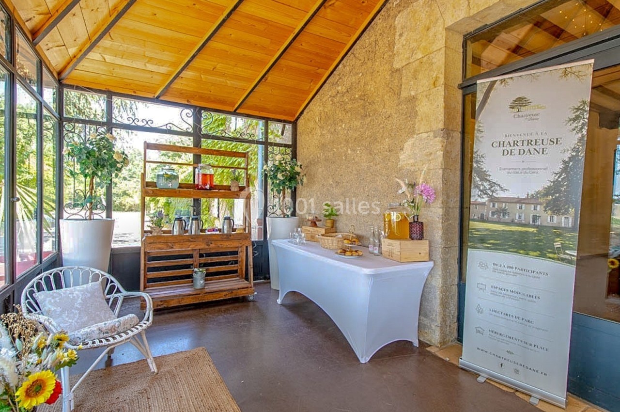 Espace lumineux avec table de buffet, présentoir à boissons et bannière promotionnelle dans une véranda en pierre et bois.