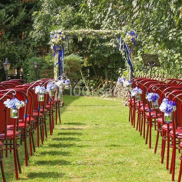Allée centrale bordée de chaises rouges décorées de fleurs bleues, menant à une arche fleurie dans un jardin.