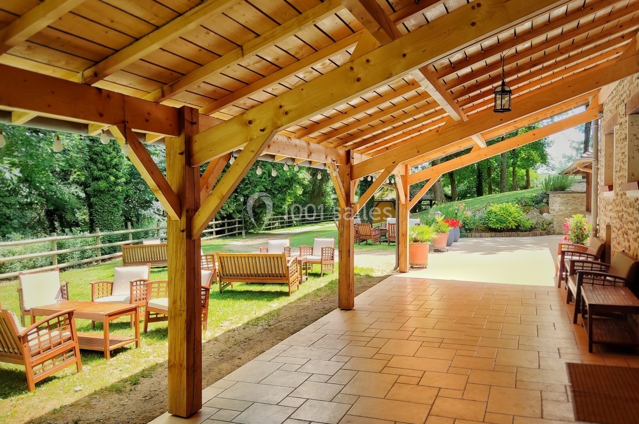 Terrasse couverte en bois avec mobilier de jardin, donnant sur un espace vert arboré et ensoleillé.