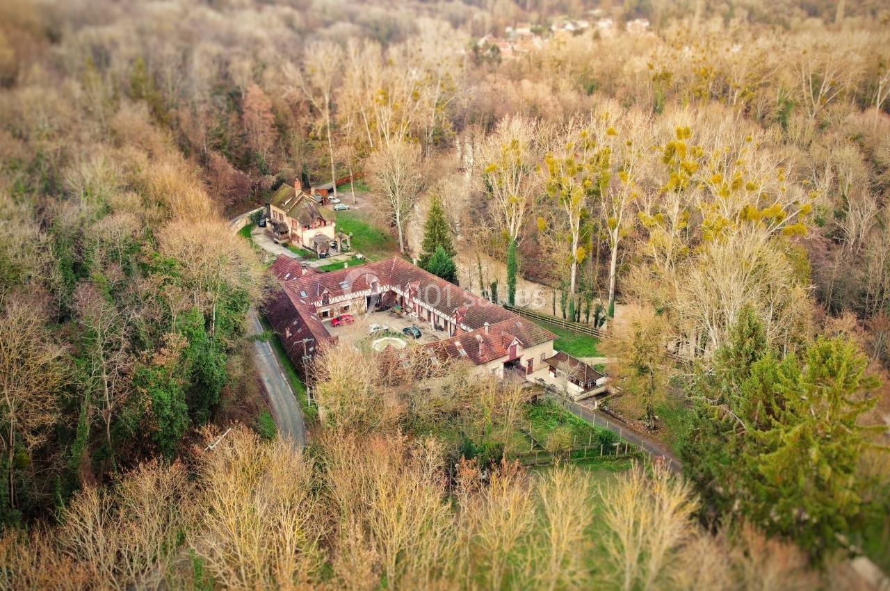 Vue aérienne d'une grande propriété entourée d'arbres en automne, avec bâtiments en tuiles rouges et une piscine.