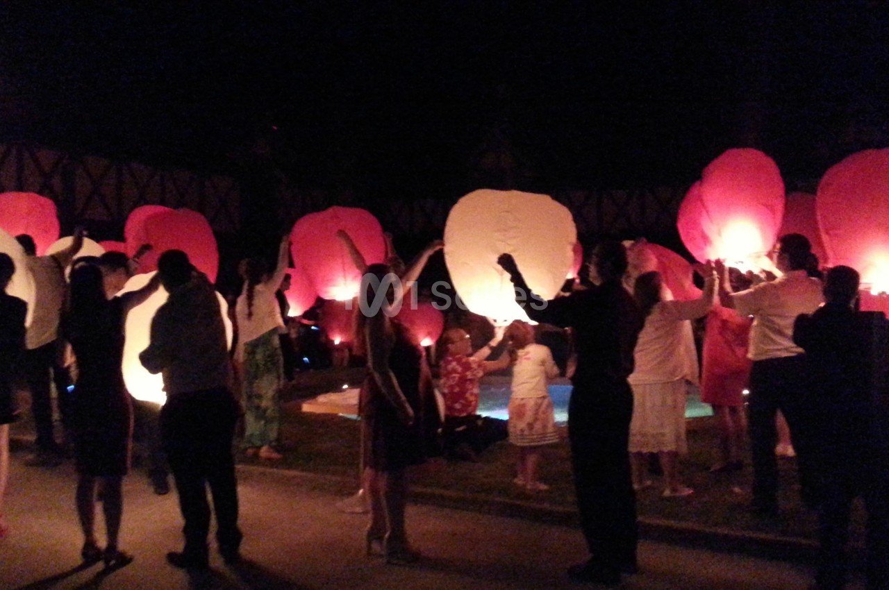 Des personnes relâchent des lanternes volantes lumineuses rouges et blanches dans la nuit.
