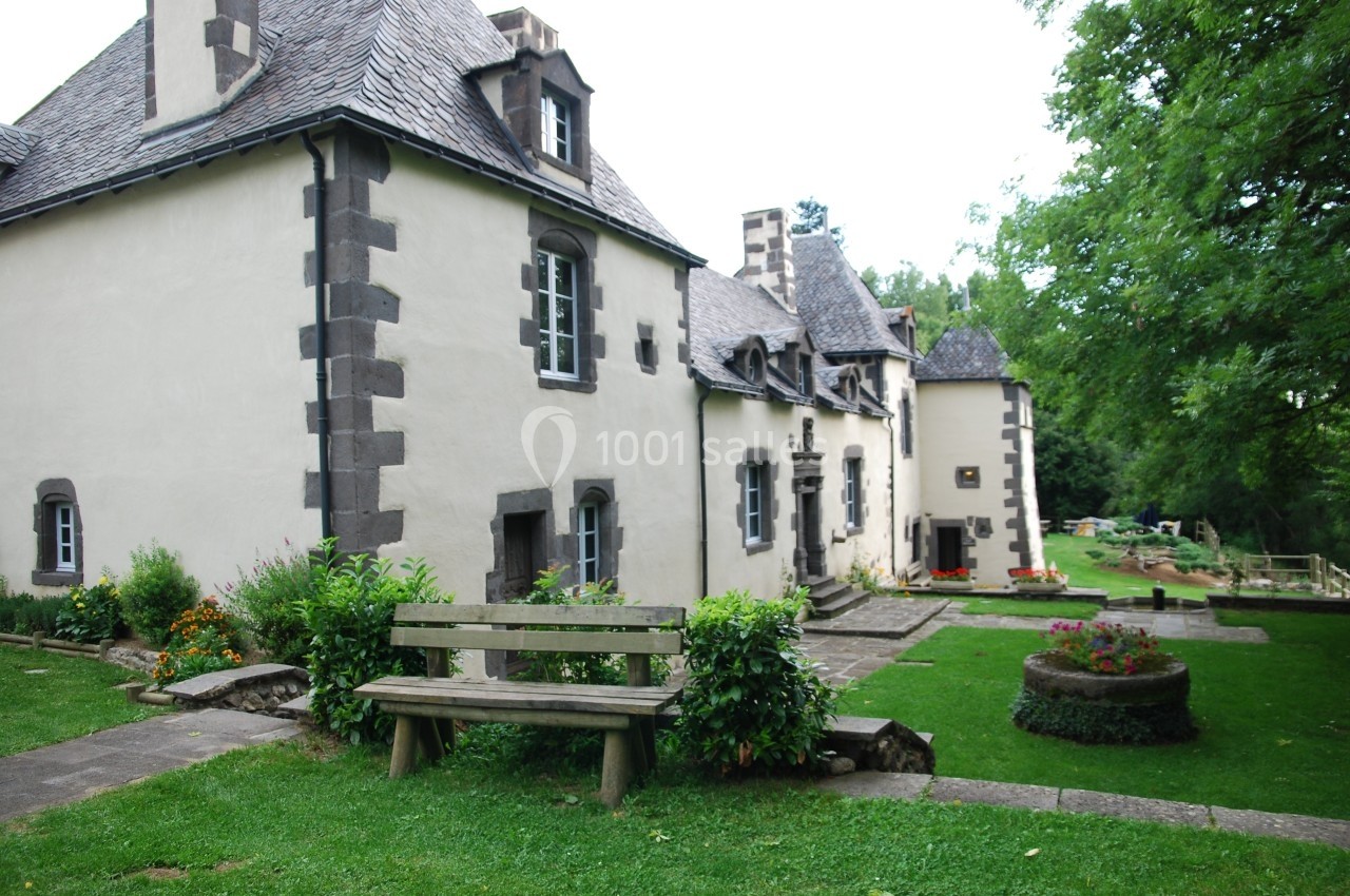 Location salle Charbonnières-les-Varennes (Puy-de-Dôme) - Manoir de Veygoux #2 Façade d'une maison en pierre avec toit en ardoise, entourée d'un jardin verdoyant et d'un banc en bois.