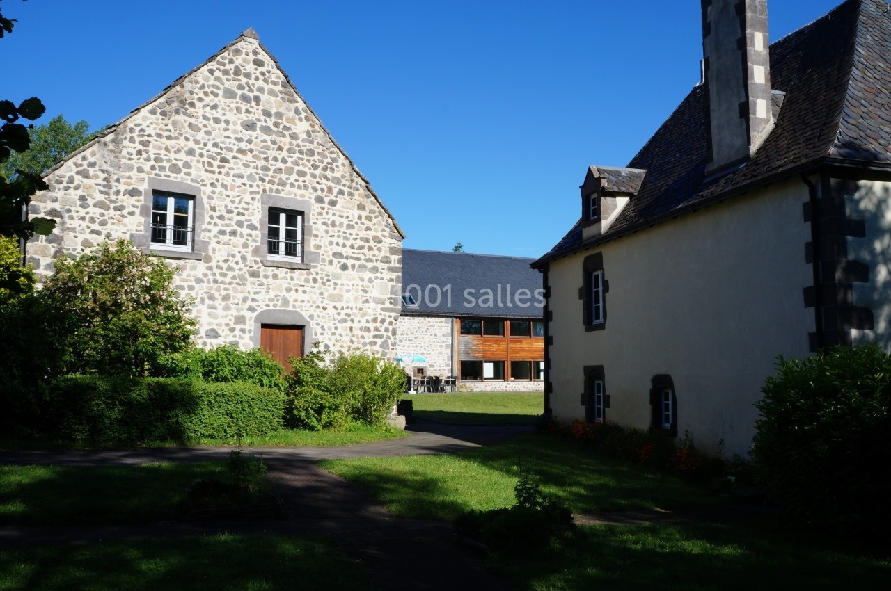 Location salle Charbonnières-les-Varennes (Puy-de-Dôme) - Manoir de Veygoux #5 Deux bâtiments en pierre avec jardin verdoyant sous un ciel bleu clair.