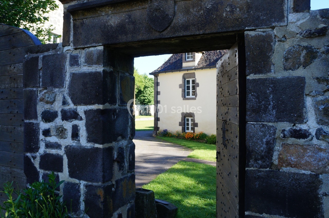 Location salle Charbonnières-les-Varennes (Puy-de-Dôme) - Manoir de Veygoux #7 Portail en pierre ouvert donnant sur une maison en pierre avec des volets blancs et un jardin fleuri.
