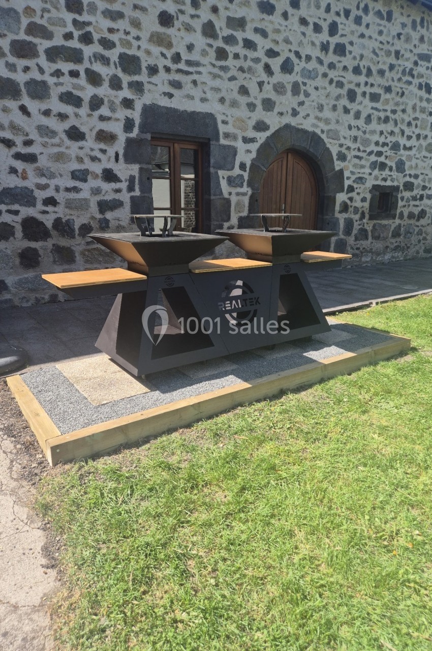 Deux barbecues modernes en métal sur une plateforme en bois devant un bâtiment en pierre.