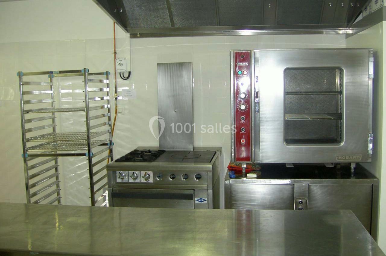 Cuisine professionnelle avec four en inox, plaque de cuisson, étagère métallique et plan de travail en acier.