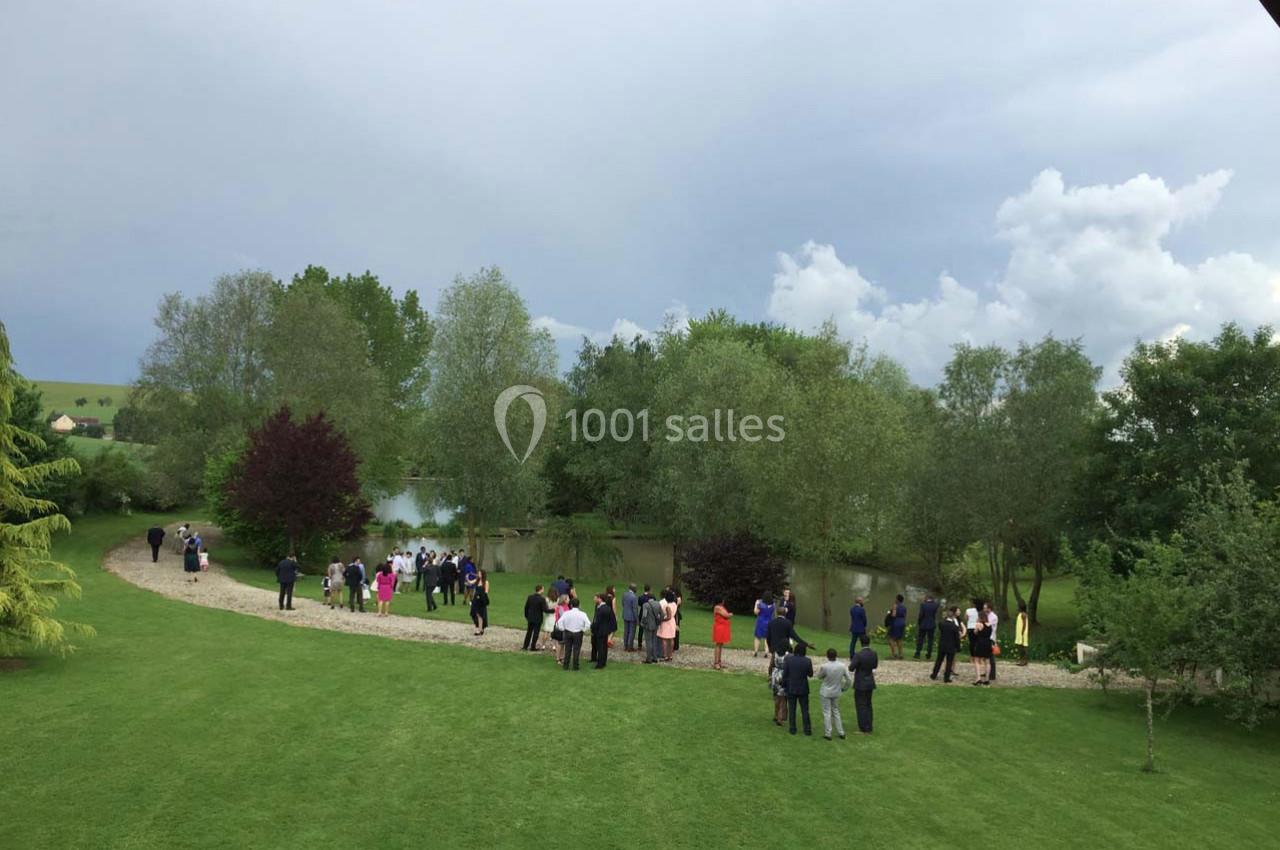 Groupe de personnes rassemblées près d'un étang dans un parc verdoyant sous un ciel nuageux.