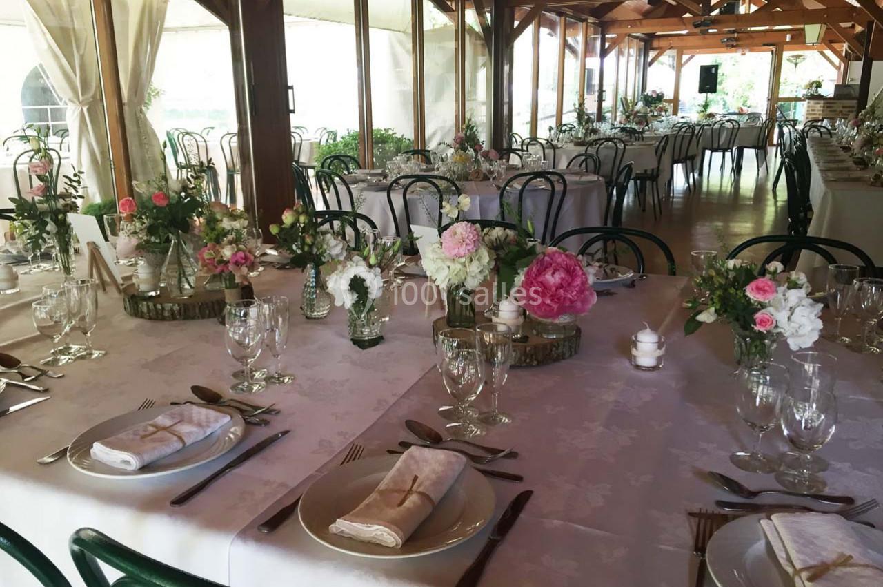 Salle de réception décorée avec des tables dressées, nappes blanches, fleurs fraîches et chaises en métal vert.