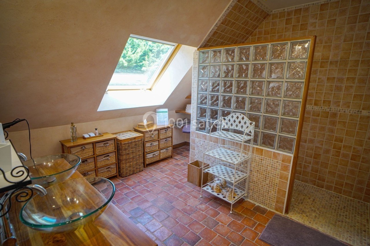 Salle de bain mansardée avec douche en briques de verre, vasques en verre, meubles en bois et fenêtre de toit.