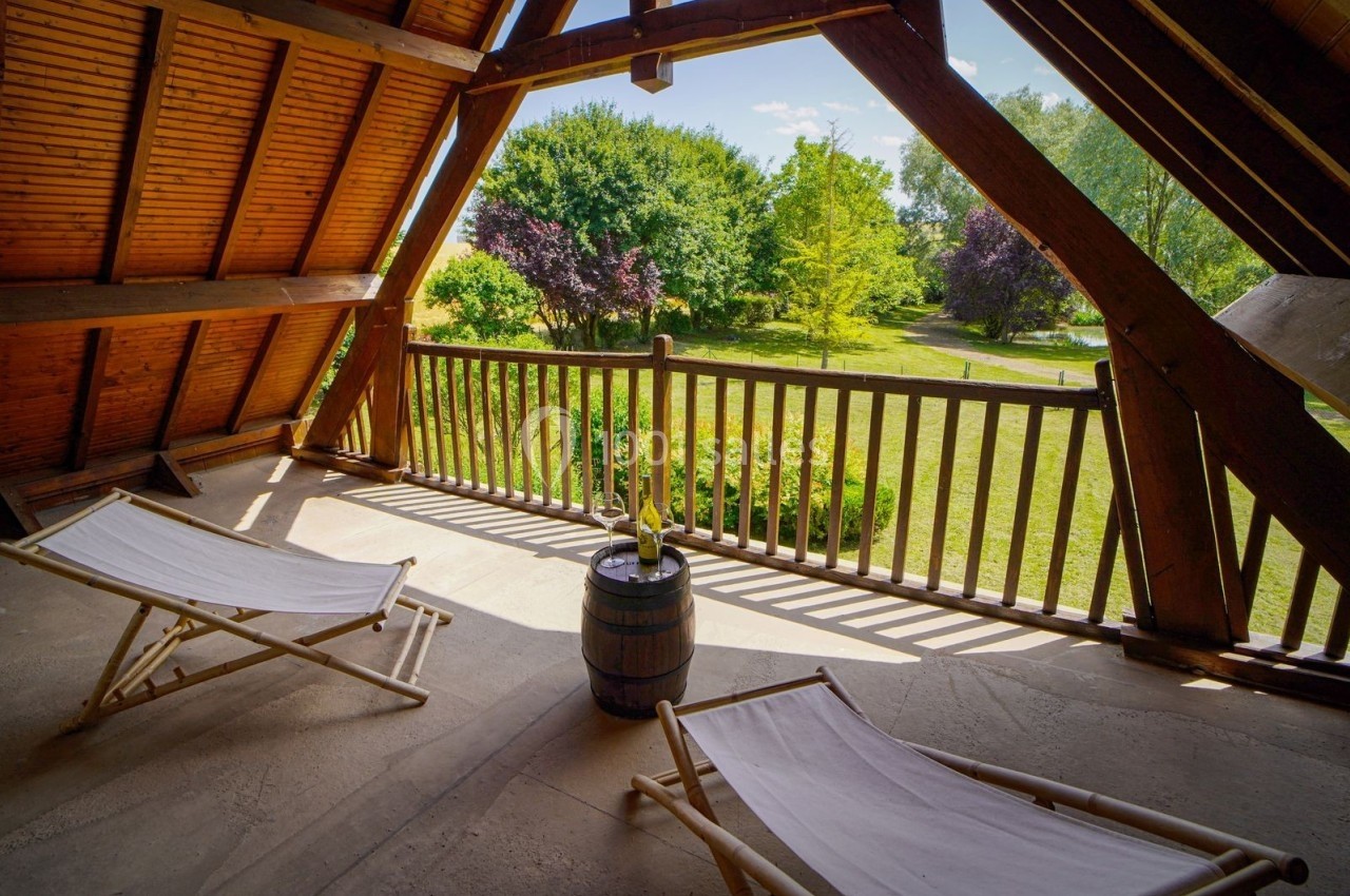 Deux chaises longues sur une terrasse en bois avec vue sur un jardin verdoyant et ensoleillé.