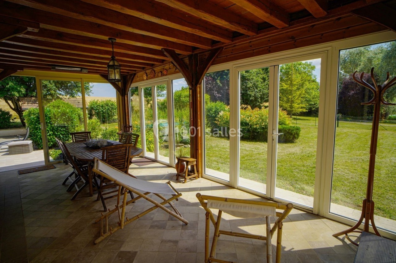 Véranda lumineuse avec mobilier en bois, donnant sur un jardin verdoyant par de grandes baies vitrées.