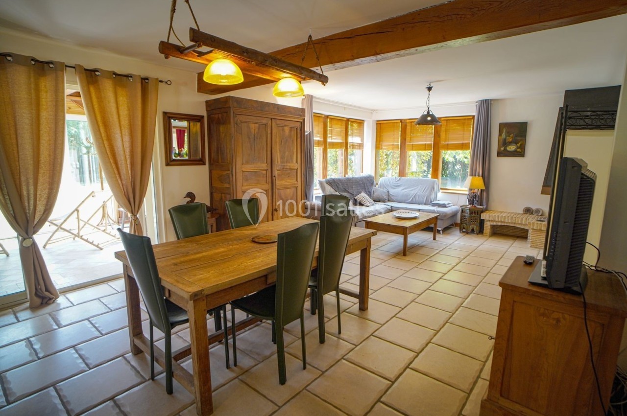 Salle à manger lumineuse avec table en bois, chaises noires, canapé, grandes fenêtres et décoration chaleureuse.