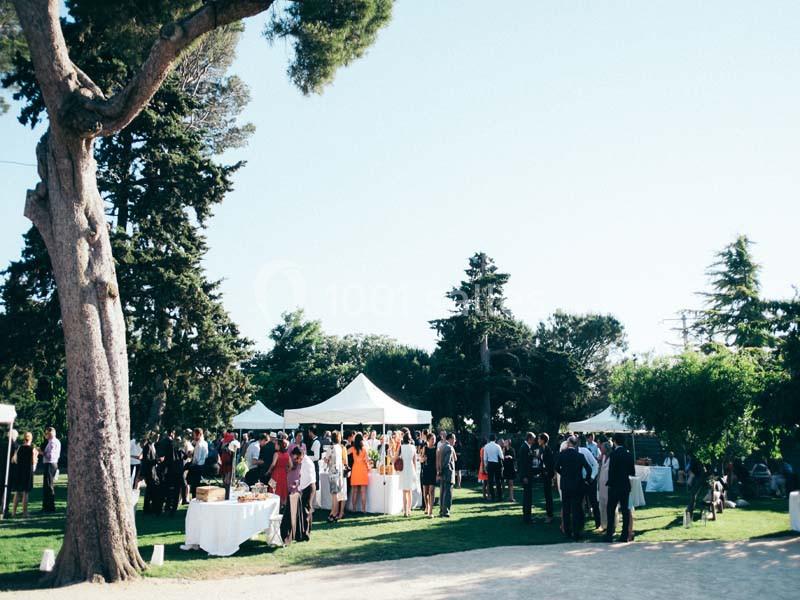 Location salle Pomérols (Hérault) - Domaine Fon de Rey #8 Groupe de personnes rassemblées dans un jardin avec des tentes blanches, entouré d'arbres et de verdure.