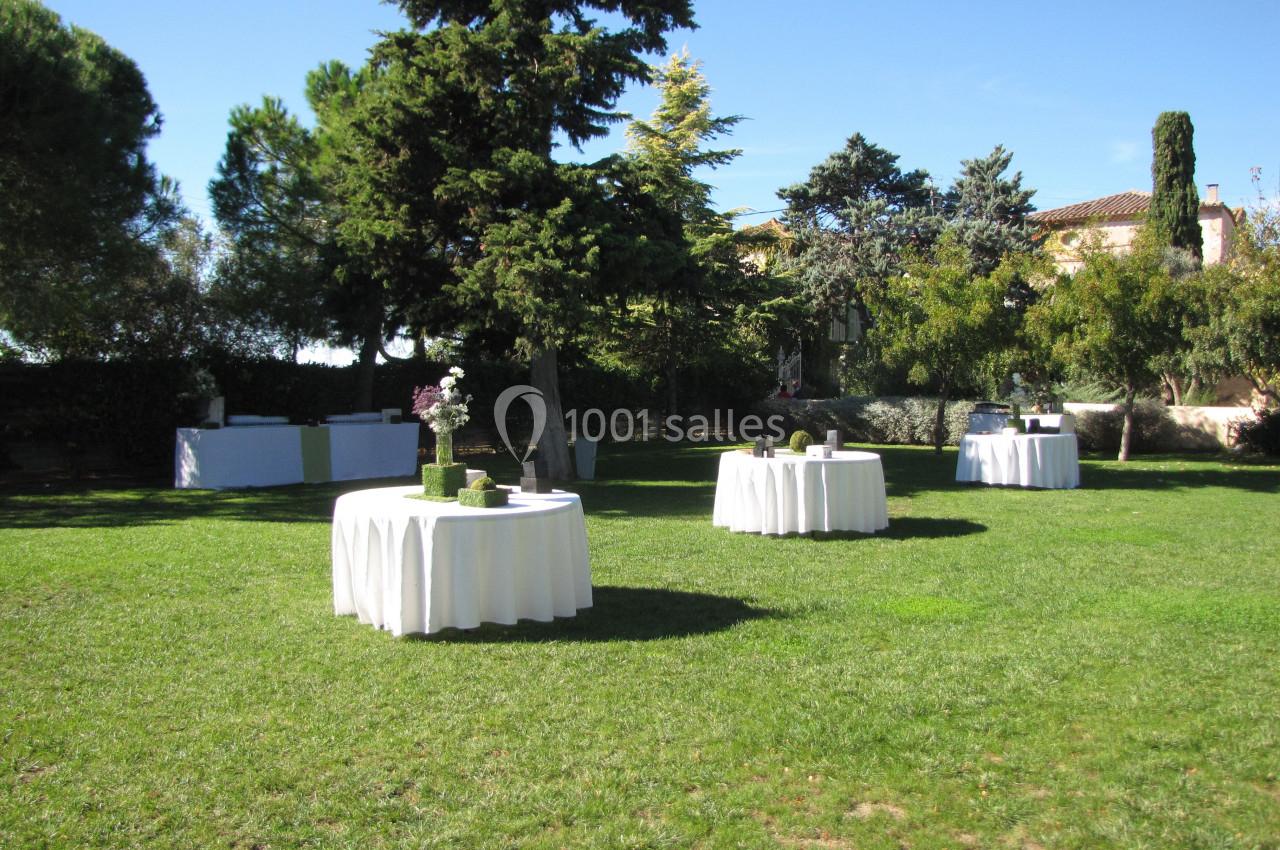 Location salle Pomérols (Hérault) - Domaine Fon de Rey #35 Tables rondes dressées avec nappes blanches sur une pelouse, entourées d'arbres et de végétation sous un ciel dégagé.