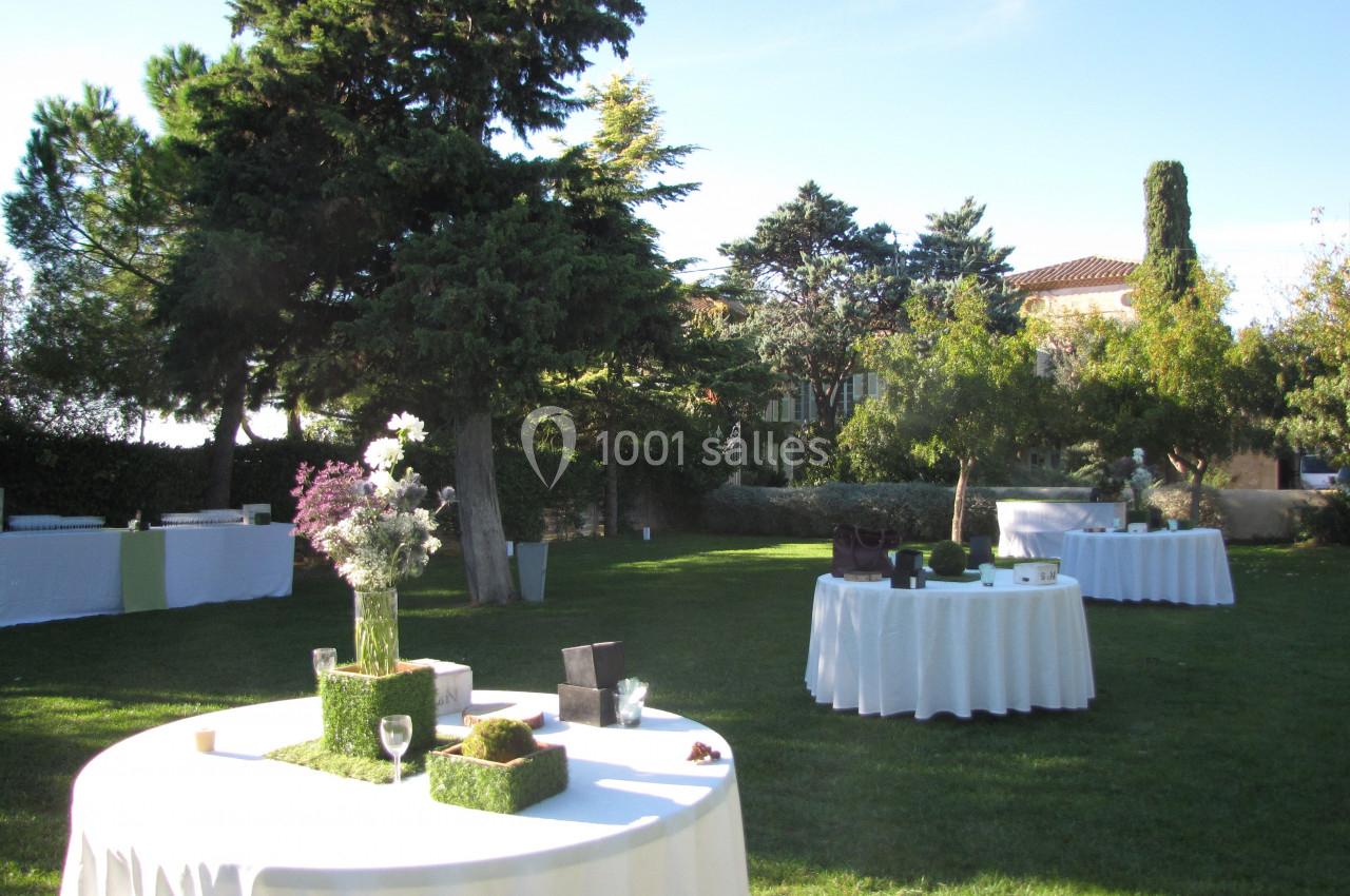 Location salle Pomérols (Hérault) - Domaine Fon de Rey #36 Tables rondes dressées avec nappes blanches dans un jardin verdoyant, entouré d'arbres et de végétation.