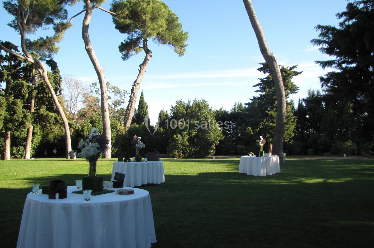 Location salle Pomérols (Hérault) - Domaine Fon de Rey #37 Tables rondes dressées avec nappes blanches sur une pelouse, entourées d'arbres sous un ciel dégagé.
