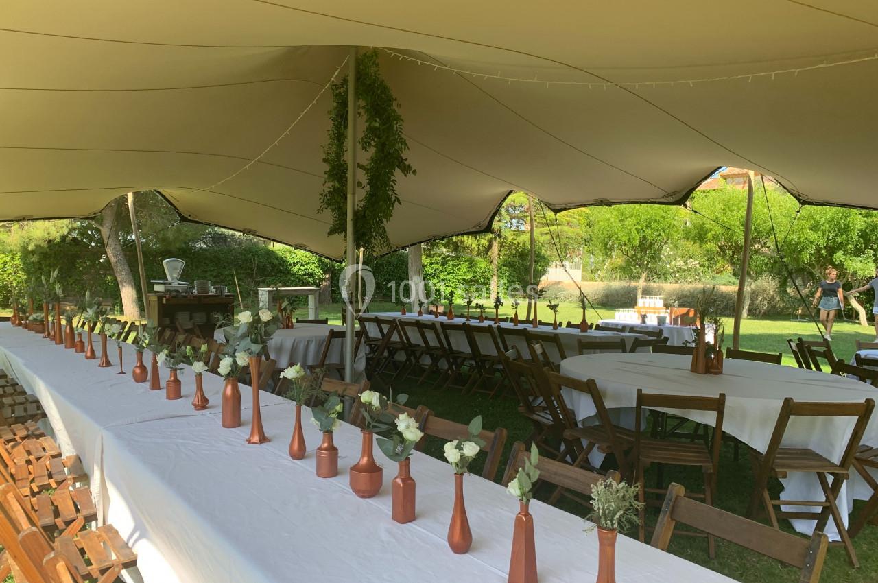 Location salle Pomérols (Hérault) - Domaine Fon de Rey #48 Tables longues décorées de vases en cuivre et fleurs, disposées sous une tente blanche dans un jardin verdoyant.