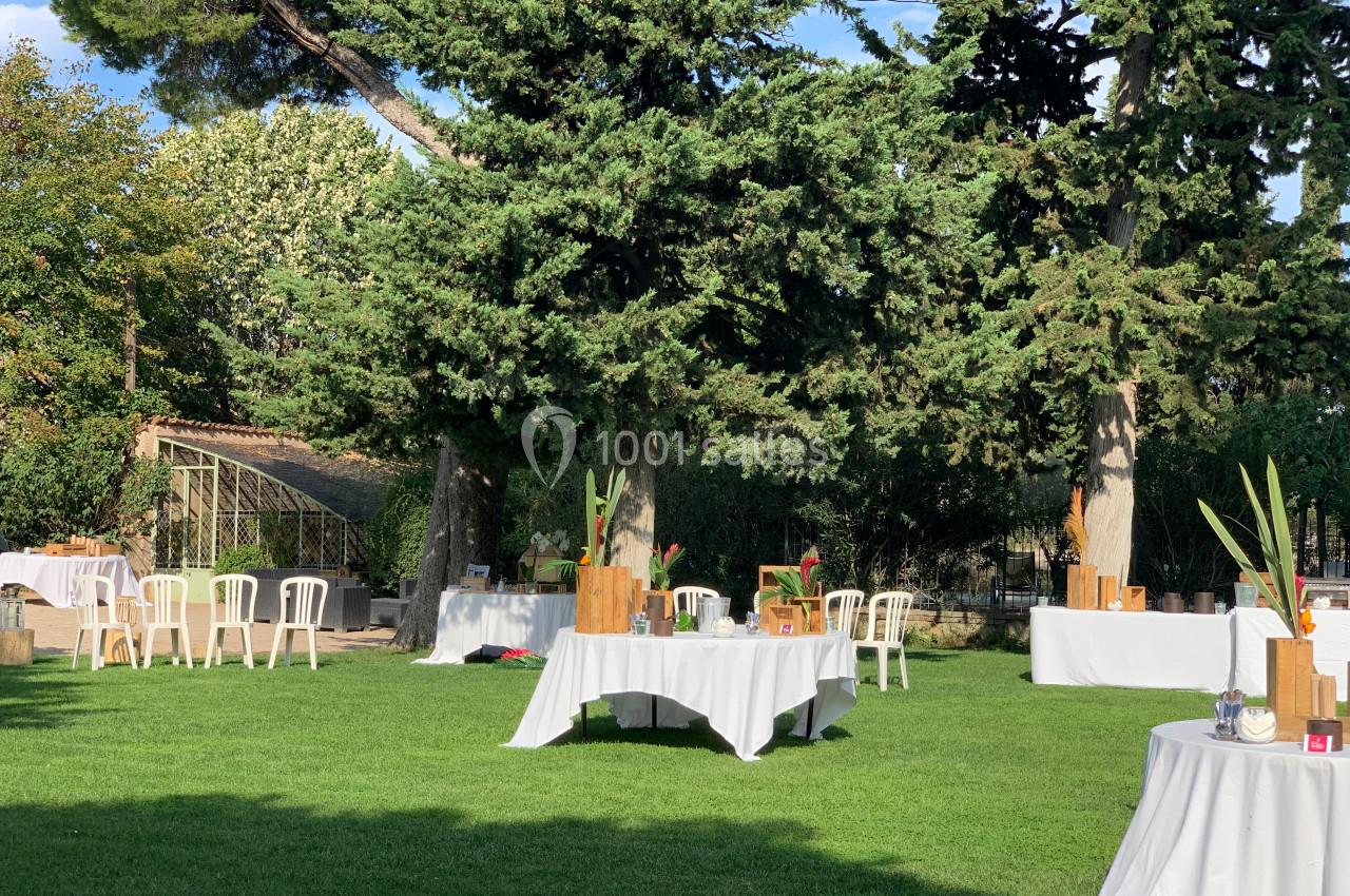 Location salle Pomérols (Hérault) - Domaine Fon de Rey #50 Tables décorées installées sur une pelouse entourée d'arbres, dans un jardin ensoleillé.