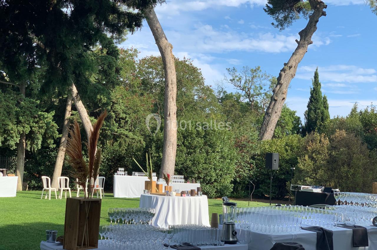 Location salle Pomérols (Hérault) - Domaine Fon de Rey #51 Tables dressées avec des verres et des décorations dans un jardin verdoyant sous un ciel bleu.