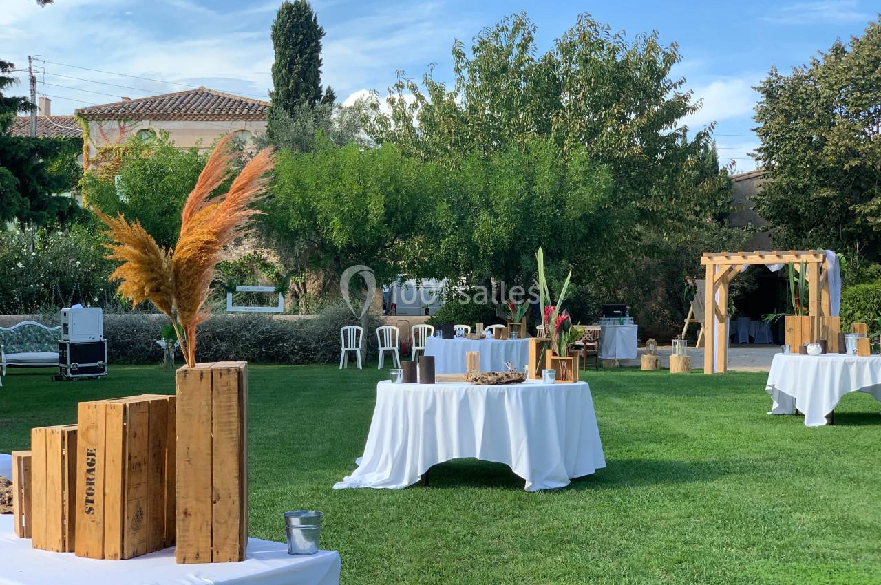 Location salle Pomérols (Hérault) - Domaine Fon de Rey #53 Tables décorées pour un événement en plein air, disposées sur une pelouse avec des éléments en bois et des plantes.