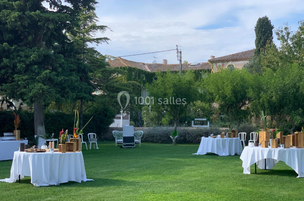 Location salle Pomérols (Hérault) - Domaine Fon de Rey #54 Tables dressées avec nappes blanches et décorations en bois disposées sur une pelouse dans un jardin arboré.