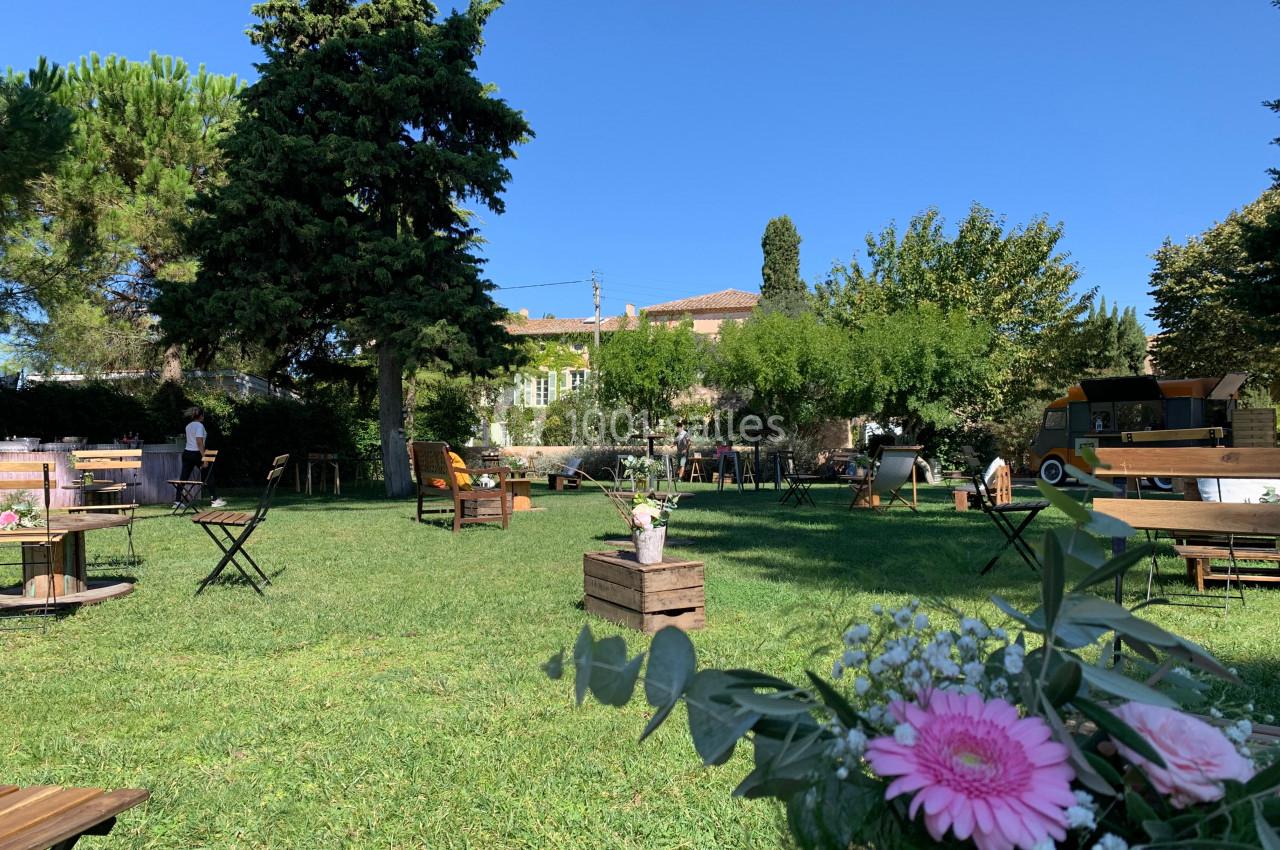 Location salle Pomérols (Hérault) - Domaine Fon de Rey #57 Espace extérieur avec tables et chaises sur une pelouse, décoré de fleurs, entouré d'arbres et de bâtiments.
