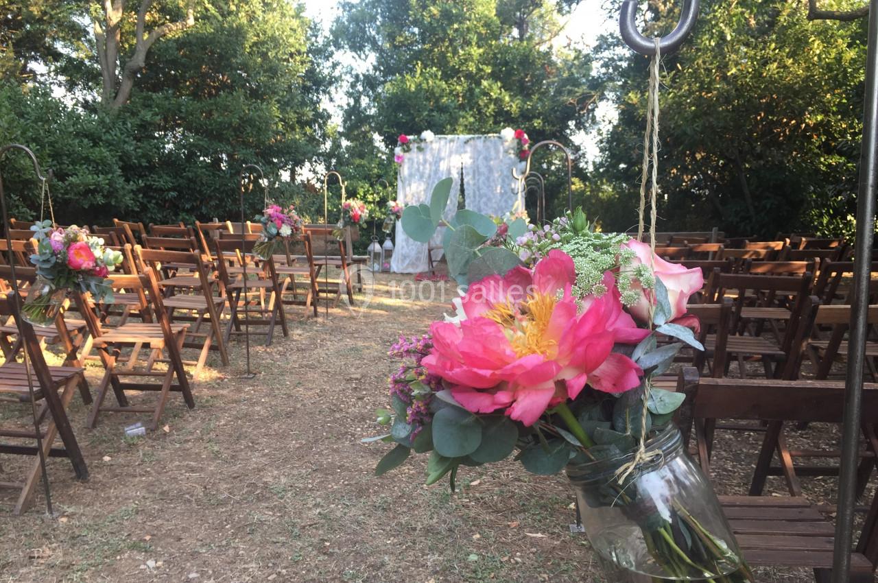 Location salle Pomérols (Hérault) - Domaine Fon de Rey #59 Allée de chaises en bois décorées de fleurs colorées, menant à une arche pour une cérémonie en extérieur.