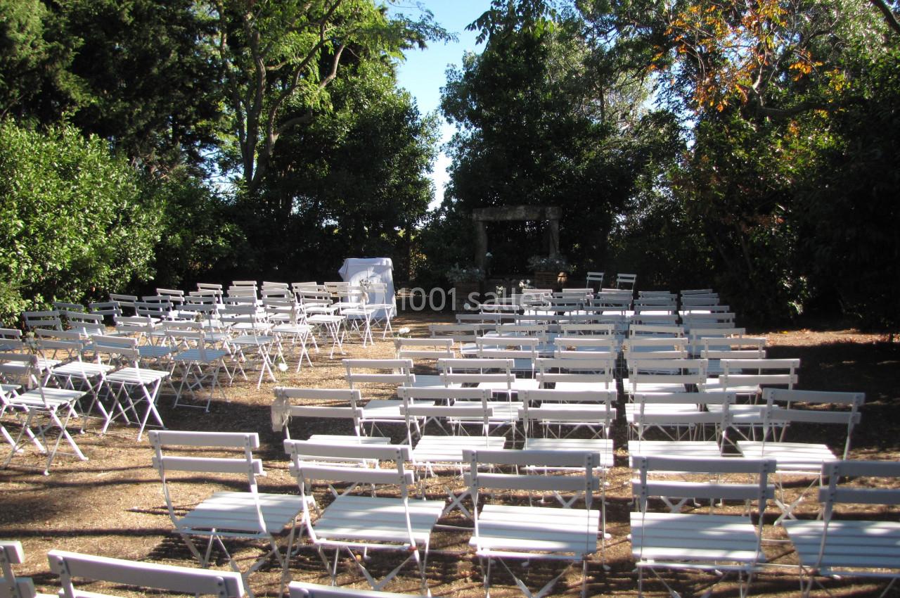 Location salle Pomérols (Hérault) - Domaine Fon de Rey #60 Chaises blanches disposées en rangées dans un espace extérieur entouré d'arbres, préparé pour un événement.