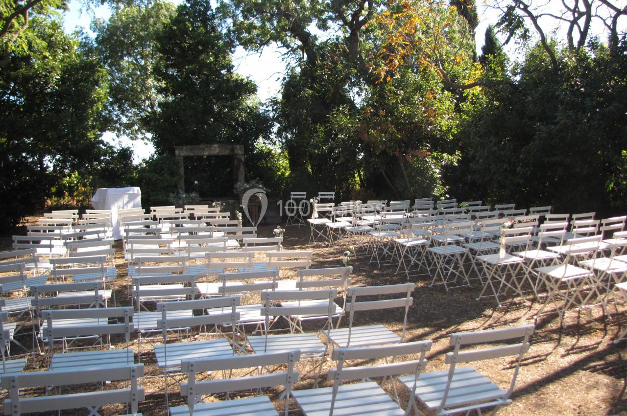 Location salle Pomérols (Hérault) - Domaine Fon de Rey #61 Chaises blanches disposées en extérieur sous des arbres, formant une configuration pour un événement ou une cérémonie.