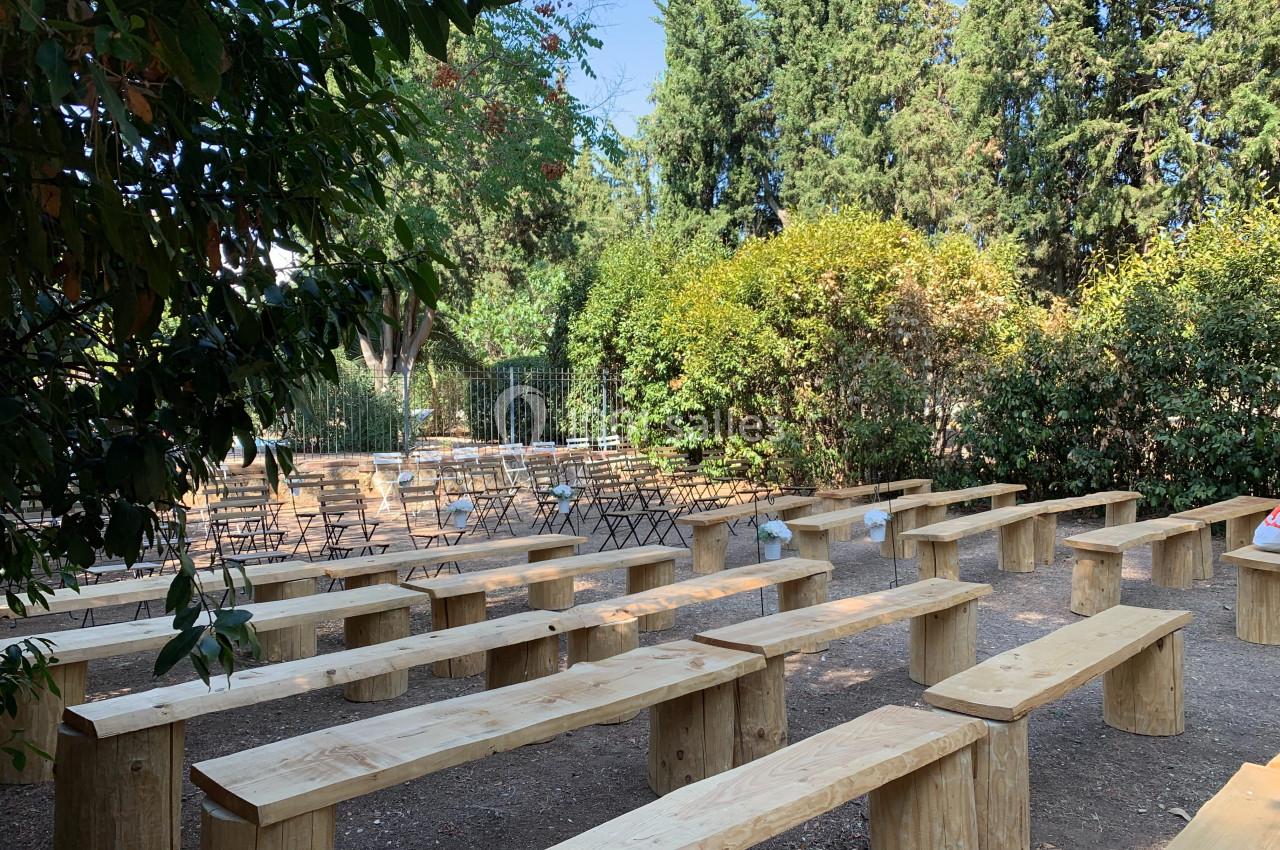 Location salle Pomérols (Hérault) - Domaine Fon de Rey #63 Bancs en bois disposés en rangées dans un espace extérieur entouré de végétation et de chaises pliantes.