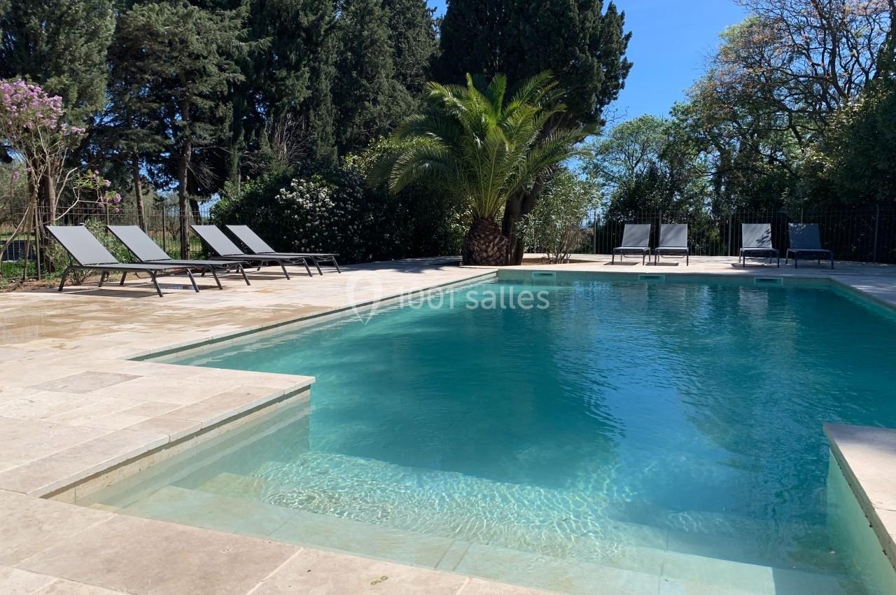 Location salle Pomérols (Hérault) - Domaine Fon de Rey #64 Piscine extérieure entourée de chaises longues, arbres et végétation sous un ciel bleu clair.