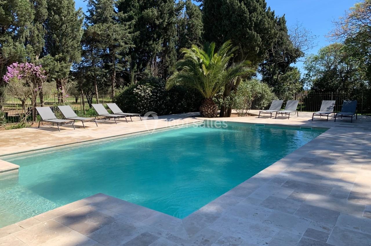 Location salle Pomérols (Hérault) - Domaine Fon de Rey #65 Piscine extérieure entourée de chaises longues, de végétation luxuriante et de grands arbres sous un ciel bleu.