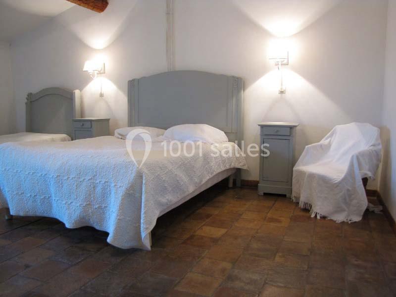 Location salle Pomérols (Hérault) - Domaine Fon de Rey #17 Chambre avec lit double, chevets assortis, fauteuil recouvert et sol en carrelage dans un décor sobre et lumineux.