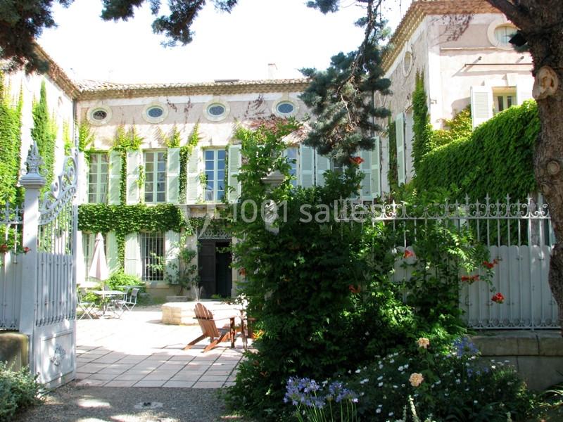 Location salle Pomérols (Hérault) - Domaine Fon de Rey #2 Façade d'une maison en pierre couverte de lierre, entourée d'un jardin avec des arbres, fleurs et mobilier de terrasse.