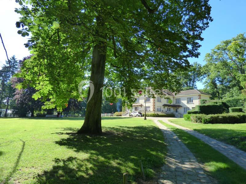 Allée pavée menant à une maison entourée de pelouses et d'arbres dans un cadre verdoyant.