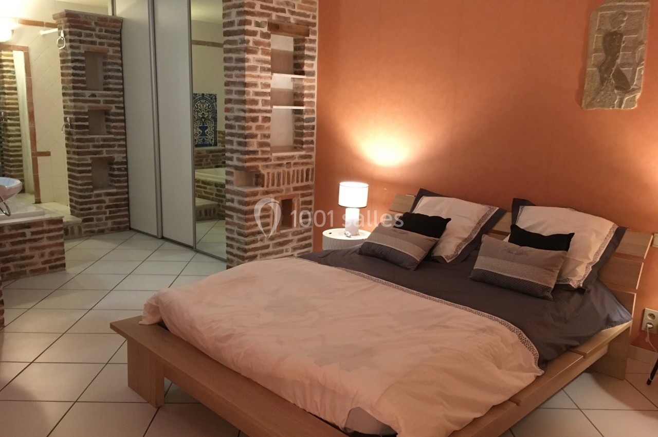 Chambre avec lit double, murs en briques et orange, éclairage doux, miroir et carrelage au sol.