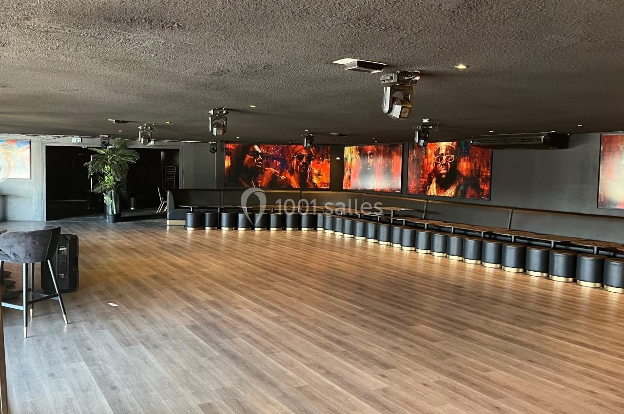 Salle spacieuse avec parquet, murs sombres, écrans lumineux et rangée de sièges noirs le long d'un mur.